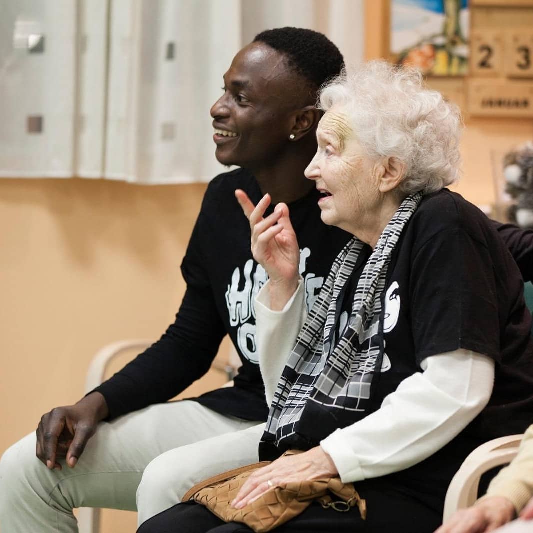 Adetayo sitting with a care-home resident, both in Homies and Omies shirts