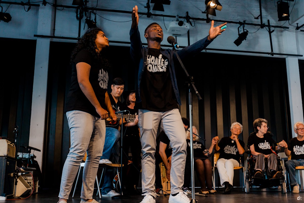 Adetayo and fellow students on stage with care-home residents at a One Community Concert