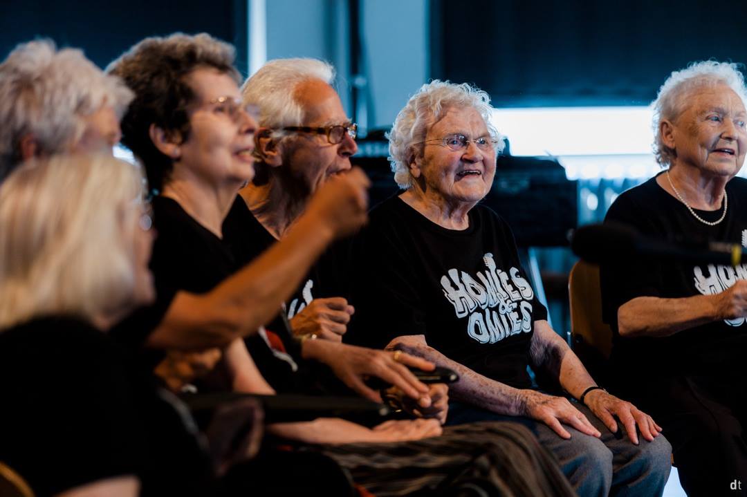Care-home residents in Homies and Omies shirts laughing in the front row of a concert